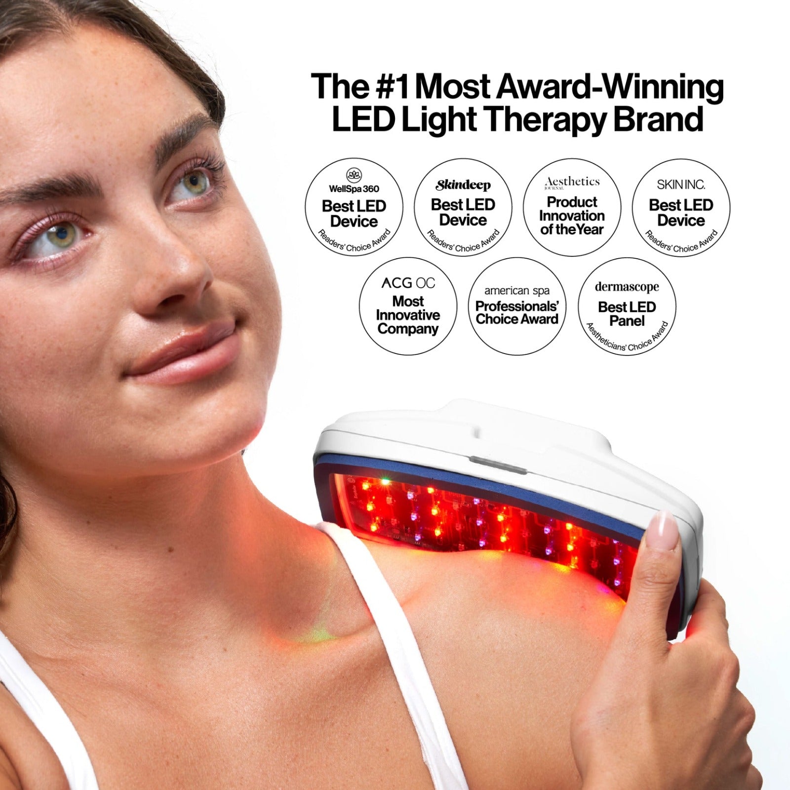Woman using a LED light therapy device with award logos displayed.